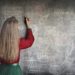 woman in red long sleeve writing on chalk board